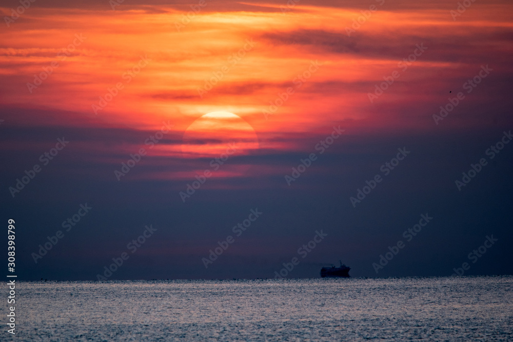 Sunset scene at the sea. Dramatic red sky above the silhouette of a ship in calm sea waters.