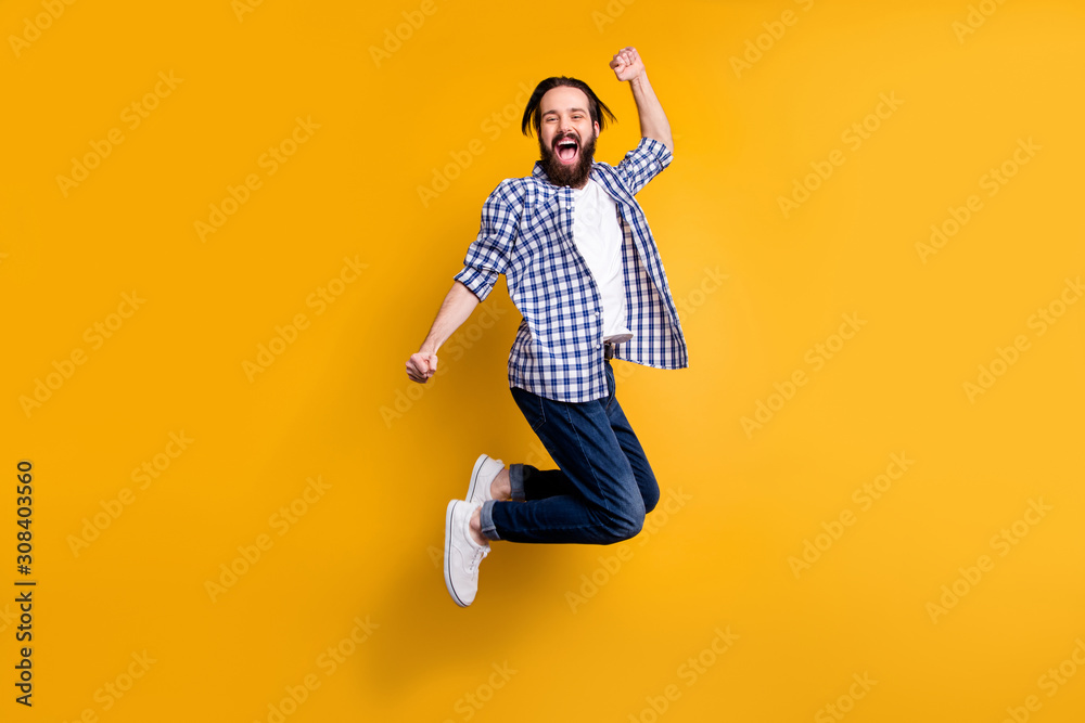 Full length body size view of nice attractive cheerful cheery bearded guy in checked shirt jumping rejoicing having fun isolated over bright vivid shine vibrant yellow color background