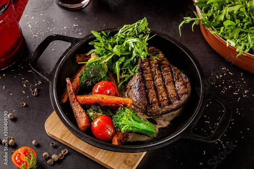 Naklejka na ścianę American food concept. Grilled beef steak with grilled vegetables, with carrots, cherry tomatoes, broccoli, in a cast iron pan. copy space
