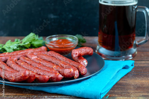 Smoked sausages on a dark plate. Nearby a large glass of dark beer. Copy space.