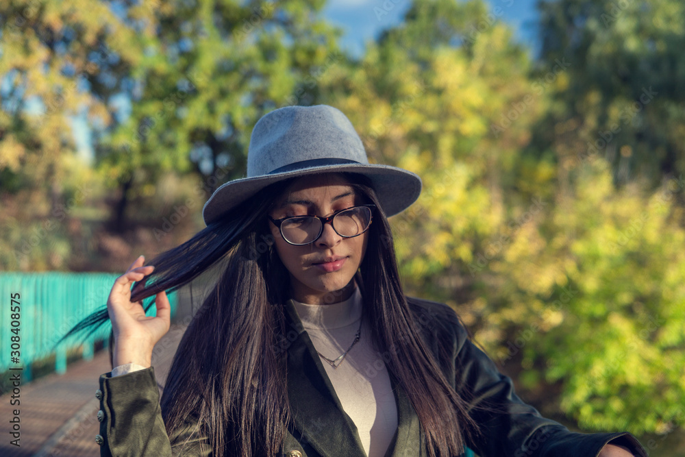 Close up of happy emotionally brunette woman with long hair and hat, smiling at camera. Beautiful model with perfect makeup after salon, posing in park. Concept of fashion and beauty.