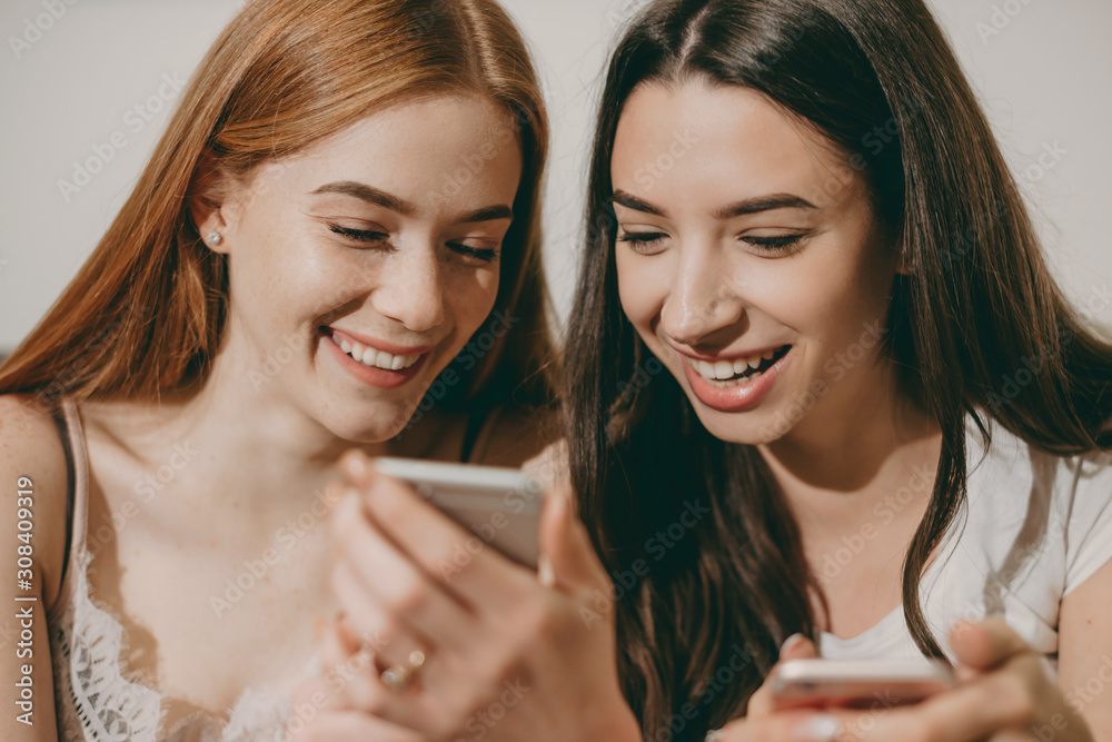 Close up portrait of a two attractive young sisters laughing while looking to a smartphone screen. Close up portrait of a two attractive young sisters laughing while looking to a smartphone screen.
