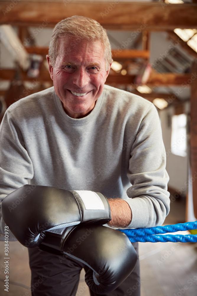 Smiling Senior Male Boxer In Gym Wearing Boxing Gloves Leaning On Ropes Of Boxing Ring Smiling Senior Male Boxer In Gym Wearing Boxing Gloves Leaning On Ropes Of Boxing Ring