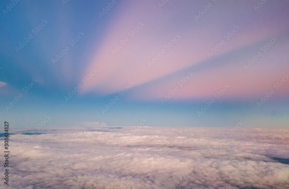 beautiful pastel sky atmosphere over white puffy cloud before sunset as seen through window of airplane, plane window. travel by airplane