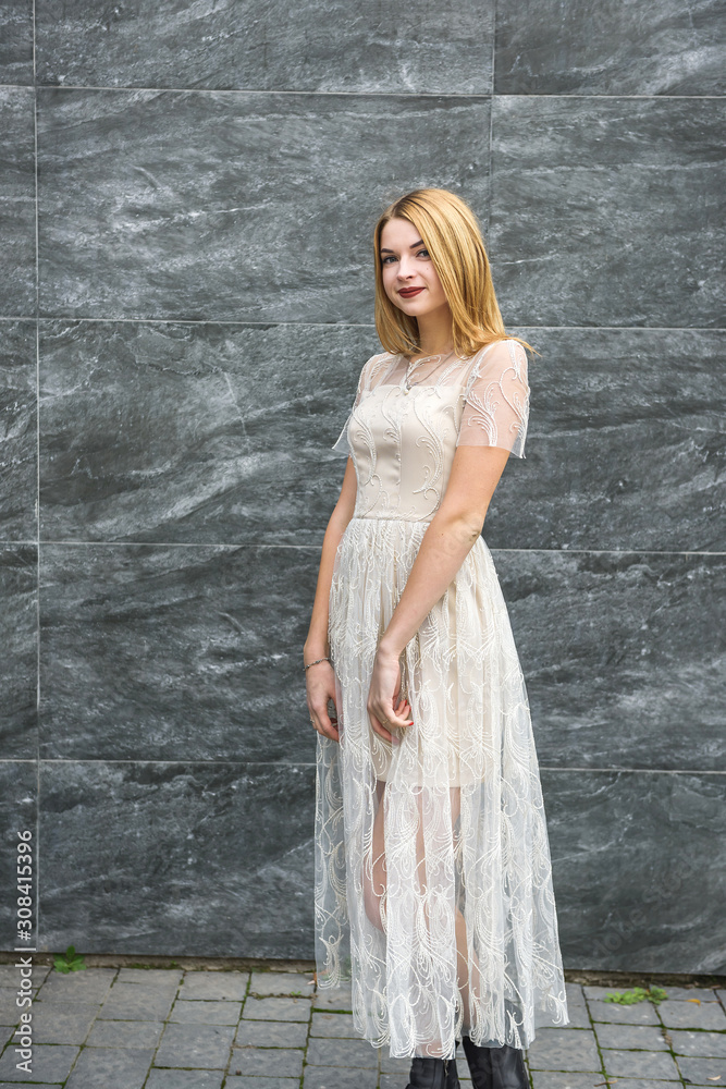 Obraz premium Young woman in evening dress posing on city street, dark wall background