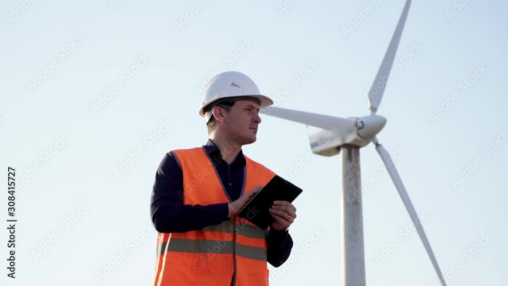 Engineer Caucasian appearance, stands near the windmill with the tablet in his hands and looks around Engineer Caucasian appearance, stands near the windmill with the tablet in his hands and looks around