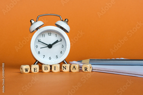 Concept webinar (online workshop, training, internet learning, teaching seminar education)  Wooden Blocks with the text: Webinar. White clock, notebook and pencil. Orange background, copy space