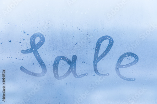 The creative inscription sale on the blue evening or morning window glass with drops 