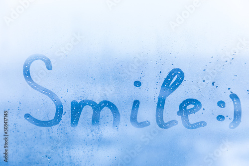 The happy child inscription smile on the blue evening or morning window glass with drops 
