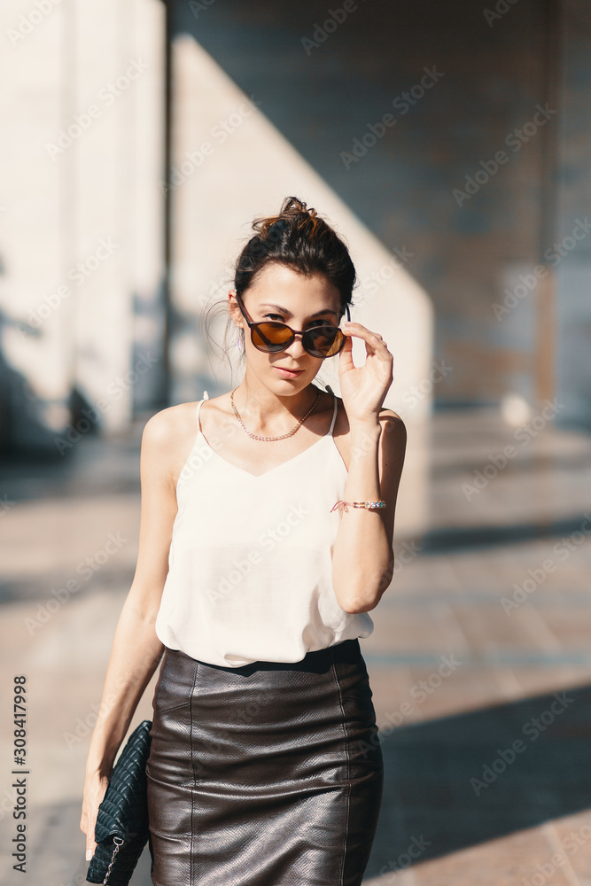 Refined business woman holding fashionable sunglasses down looking above them on blurred background