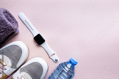 Top view of sport accessories for fitness and running. Training shoes, towel, fitness bracelet watch and water isolated on pink background.