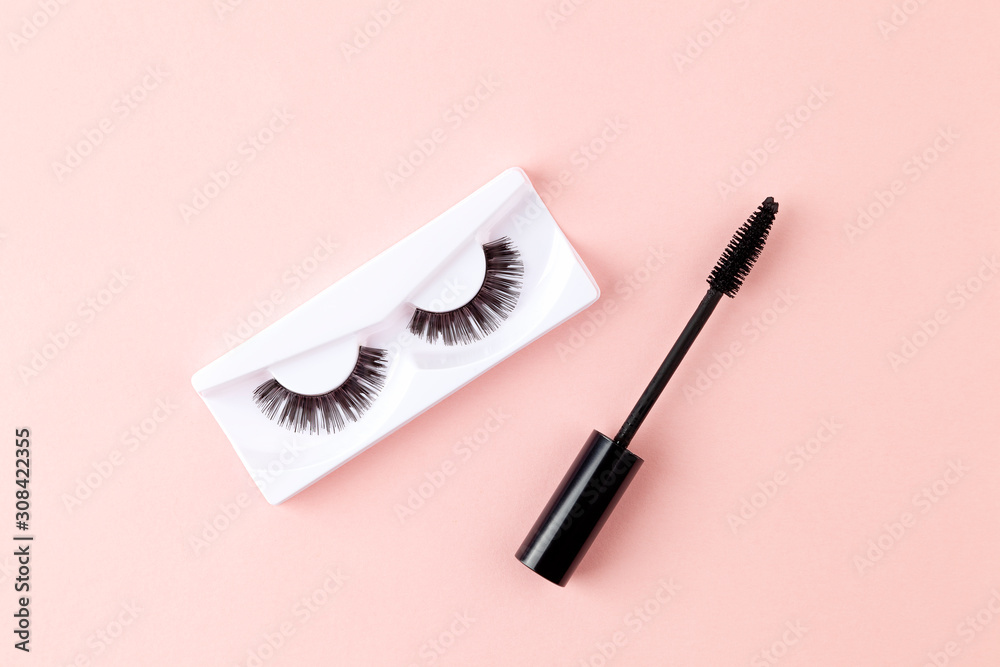 Obraz premium Women's eyelashes and brush on a pink background. Top view of Mascara brush and long false lashes. Eyelash extension, beauty blog concept. 