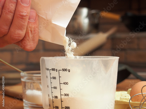 Pouring flour into measuring cup. Making yeast pancakes (crepes). photo