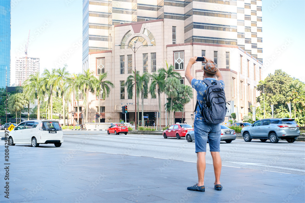 Obraz premium Man tourist travel and photo for social media in Kuala Lumpur, Malaysia. Man tourist taking photo of the city by mobile phone.