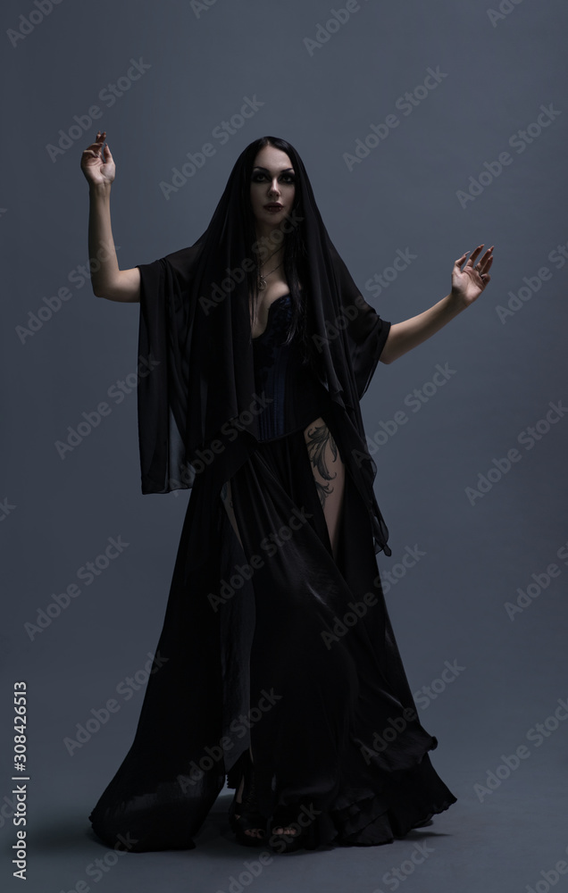 Beautiful brunette woman with gothic makeup wearing stylish black dress and posing on grey background Beautiful brunette woman with gothic makeup wearing stylish black dress and posing on grey background