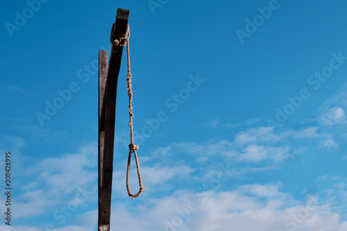 Wooden gallows with old rope and noose against cloudy sky
