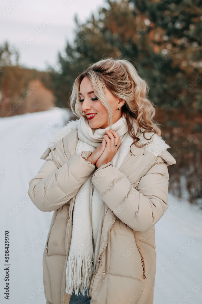 Happy attractive beautiful lonely blonde in a white sweater, warm jacket and jeans walks, enjoys freedom and tranquility on a snowy road in the forest in winter. Happy attractive beautiful lonely blonde in a white sweater, warm jacket and jeans walks, enjoys freedom and tranquility on a snowy road in the forest in winter.