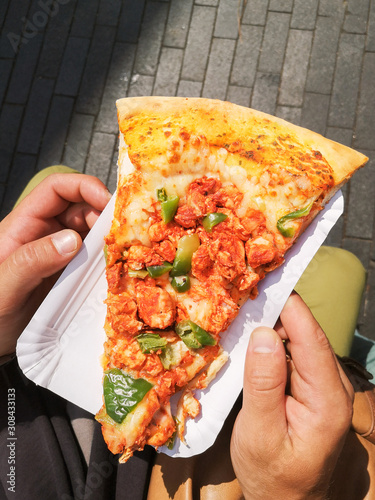 Big delicious piece of pizza in men's hands,  with jalapeño, cheese, meat, chicken, street european food. Quick snack for tourist