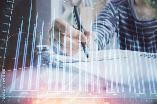 Financial forex graph drawn over hands taking notes background. Concept of research. Double exposure