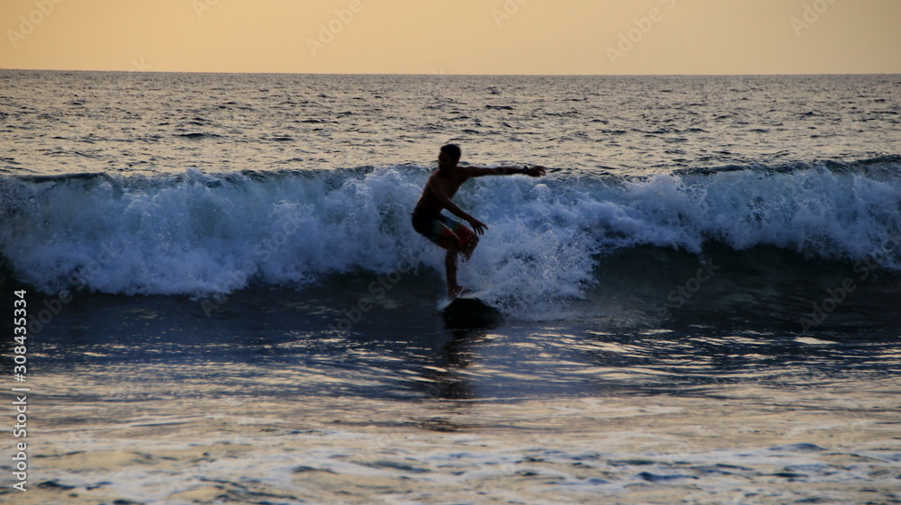 Documentation of surfers in action at dusk with a golden color and dark, unfocused and dark on the beach of Senggigi Lombok, West Nusa Tenggara Indonesia, 27 November 2019