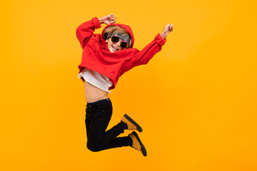 handsome boy with a bandana on his head in a red hoodie with glasses jumps on an isolated orange background