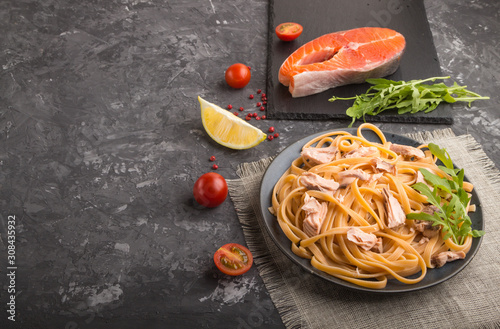 Semolina pasta with salmon and salmon steak on a black concrete background. Side view, copy space.