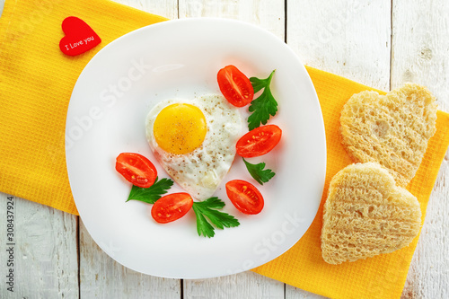 A plate of tomatoes, fried egg and heart shaped bread. Festive romantic food.