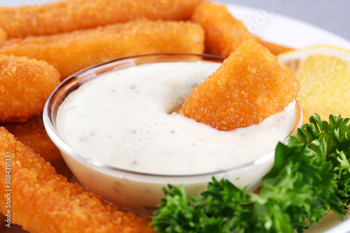 Fish fingers sticks on a plate with parsley, lemon and tartar sauce.