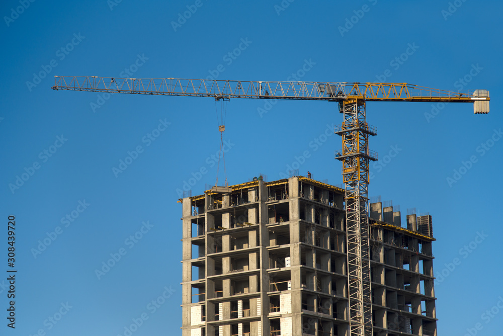Tower cranes constructing a new residential building at a construction site against blue sky. Renovation program, development, concept of the buildings industry. Tower cranes constructing a new residential building at a construction site against blue sky. Renovation program, development, concept of the buildings industry.