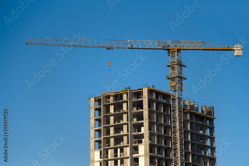 Tower cranes constructing a new residential building at a construction site against blue sky. Renovation program, development, concept of the buildings industry.