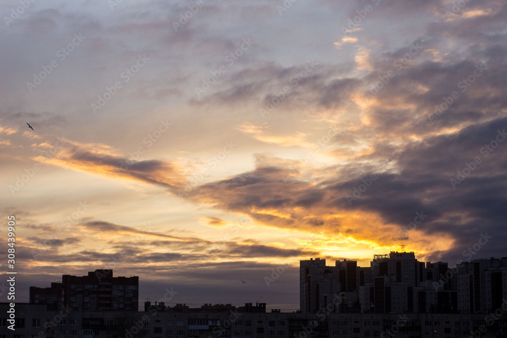 city dawn with cloudy sky in gold and gray-blue, the sun behind the clouds