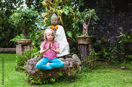 Young girl meditating in yoga lotus pose with namaste hands.