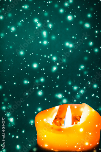 Canvas Print Orange holiday candle on green sparkling snowing background, luxury branding des
