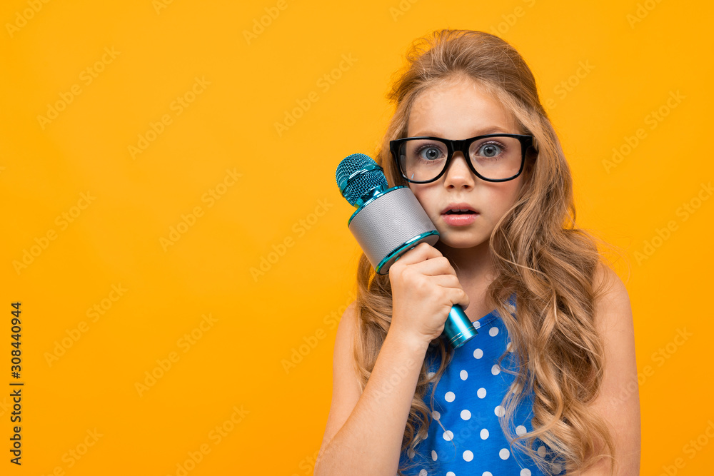 A little girl with glasses with a microphone is interviewed, the picture is isolated on yellow background A little girl with glasses with a microphone is interviewed, the picture is isolated on yellow background