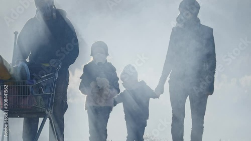 Survivor family in gas mask going through clouds of toxic smoke in desolate and burned out forest landscape.
