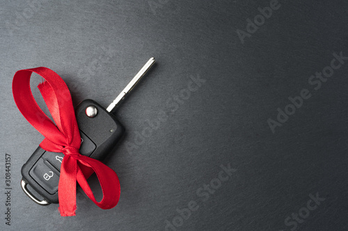 Obraz na płótnie Car key with red bow on dark black slate plate background. Christmas or Valentine's Day gift or present abstract concept. Copy space on the right. Flat lay top view. w salonie
