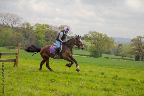 Pretty young rider and her horse galloping across the English countryside during a eventing competition.