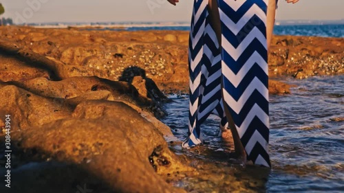 Female with long striped dress walking in shallow water at stone beach, Low close up photo