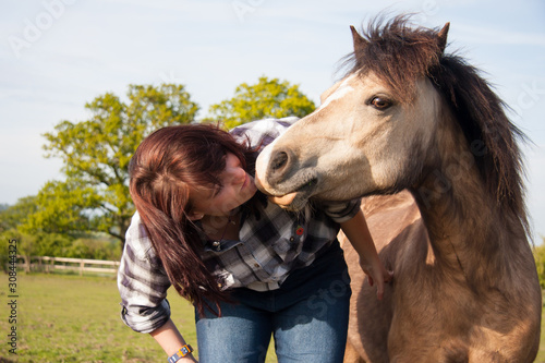 lovng moment between young woman and her pretty pony in field.