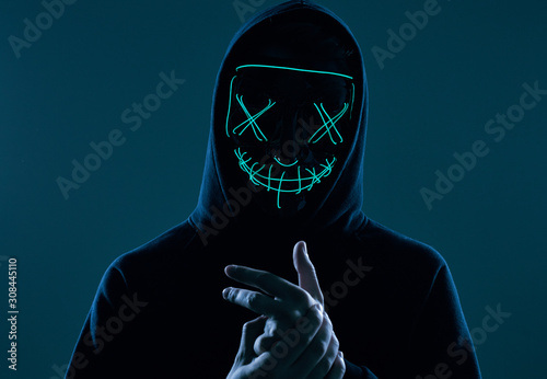 Anonymous man in black hoodie hiding his face behind a neon mask photo