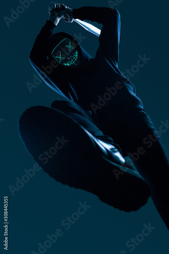 Anonymous criminal man with baseball bat in a black hoodie and neon mask photo