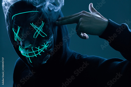 Anonymous man in black hoodie hiding his face behind a neon mask photo