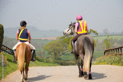 Rear view of two riders and their horses complete in safety gear enjoying riding on the country lanes of Shropshire UK.