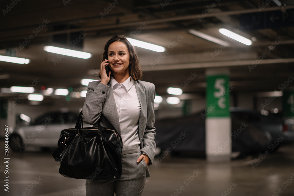 Fototapeta premium Young woman talking on phone on parking 