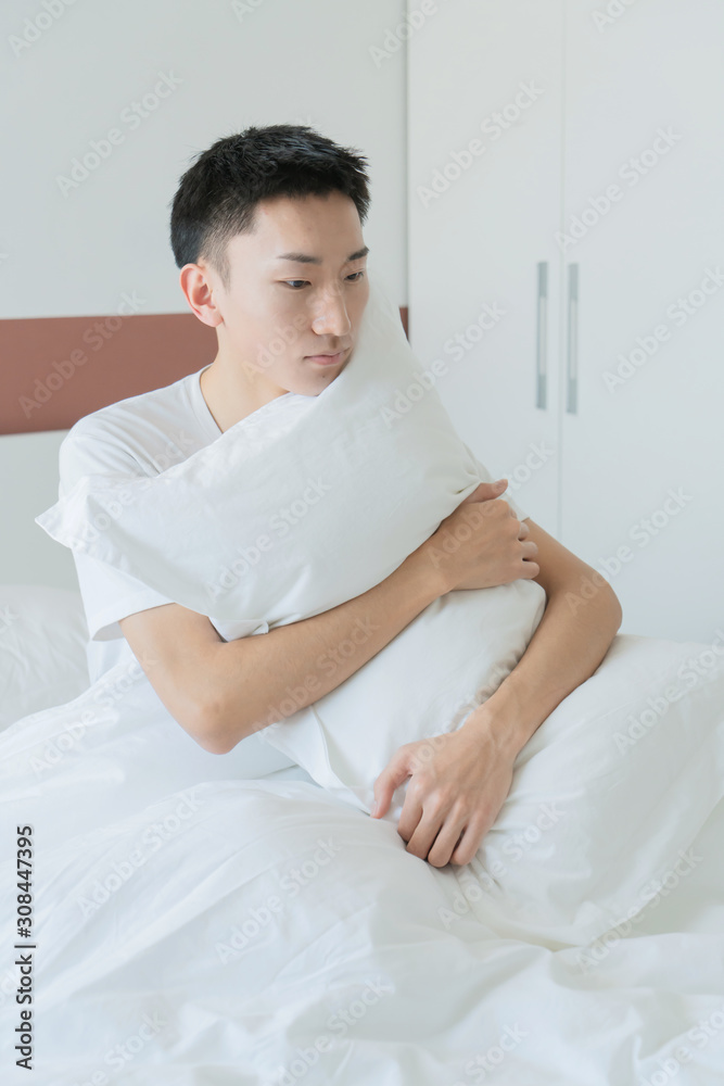 asian young man holding pillow in bedroom in the morning asian young man holding pillow in bedroom in the morning
