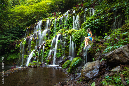 Young Caucasian woman sitting on the rock and enjoiyng waterfall landscape. Travel lifestyle. Banyu Wana Amertha waterfall Wanagiri, Bali. photo