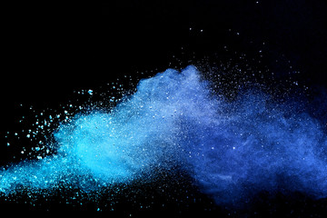 Abstract brown powder explosion. Closeup of blue dust particle splash isolated on black background.