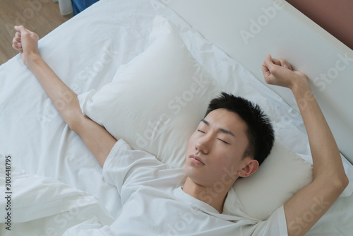 a young man waking up in bed and stretching his arms