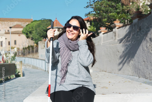 Fototapet Blind woman with a white cane using a smartphone to listen some messages