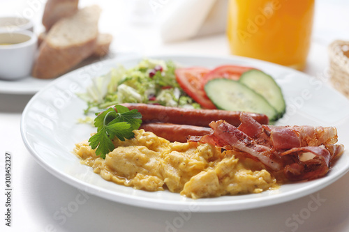 Breakfast scrambled eggs, sausage, fried bacon served with fresh vegetables.